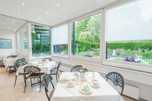 une salle à manger avec des tables blanches, des chaises et des fenêtres dans l'établissement Hotel Villa am Kurpark, à Bad Homburg vor der Höhe