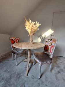 a table with two chairs and a vase on it at La chambre Mademoiselle Causeuse in Malville