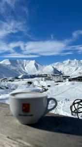 a cup sitting on a table with a view of snow covered mountains at White Tiger in New Gudauri II in Gudauri