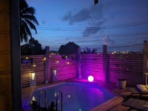 uma piscina com luzes cor-de-rosa num quintal à noite em Au cœur du papillon piscine privée em Goyave