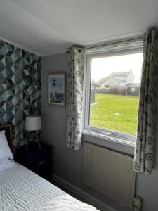 een slaapkamer met een raam met een bed en een groen veld bij Modern Funky Private Chalet at the Beach in Tywyn