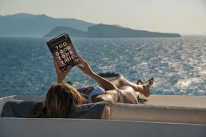 Una donna sdraiata su una barca che legge un libro di Onar Suites & Villas a Karavostasi