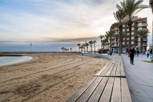 a man walking on a beach next to a wooden bench at Sunrise Horizon in Torrevieja