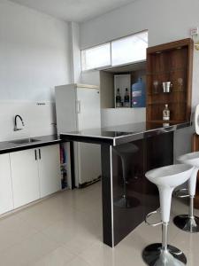 a kitchen with a black counter and white stools at Casa Blanca cerca al Mar in Máncora