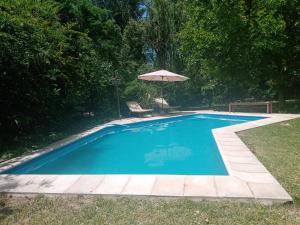 a blue swimming pool with an umbrella and a chair at La Chacrita in Chacras de Coria