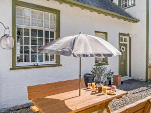 a wooden bench with an umbrella in front of a house at 2 Bed in Glen Clova 93001 in Kirriemuir