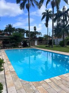 a large blue swimming pool with palm trees in the background at Villa Tavares - casa com piscina na praia da Lagoinha in Ubatuba