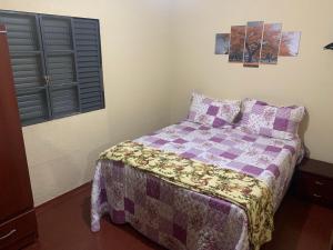 a bedroom with a bed with a purple comforter and a window at Apt térreo com 3 qtos e 1 vaga in Poços de Caldas
