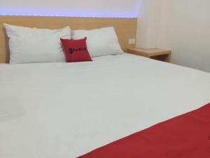 a white bed with a red pillow on it at RedDoorz Syariah @ Gedong Air Lampung in Kedaton