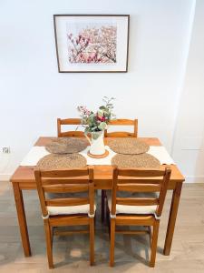 a wooden table with four chairs and a vase with flowers at Céntrico piso con parking disponible by beBalmy in Málaga