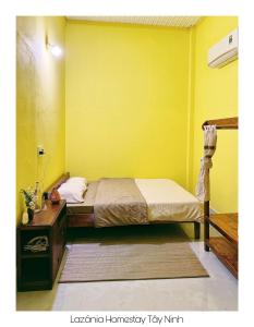 a yellow room with a bed and a table at Lazánia homestay Đất Thánh-số 8a hẻm số 3 Phạm Văn Xuyên in Tây Ninh
