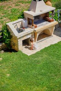 a little girl sitting in front of an outdoor oven at Houmis Apts & Studios in Agios Georgios Pagon