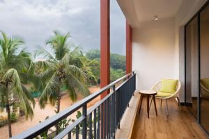 The Astor - All Suites Hotel Candolim Goa في كاندوليم: شرفة مع كرسي وإطلالة على الشاطئ