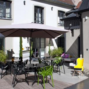 un patio con mesas, sillas y una sombrilla en Hôtel Quatorze en Colmar