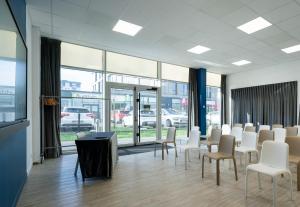 une salle de conférence avec des chaises blanches, des tables et des fenêtres dans l'établissement B&B HOTEL Saint-Nazaire Pornichet, à Saint-Nazaire