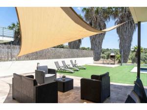 eine Terrasse mit Stühlen und eine Liegewiese mit Bäumen in der Unterkunft Villa Golf and Pool Oasis in Catllar