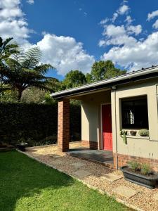 a house with a red door and a grass yard at The Aloe Garden Cottage in Howick