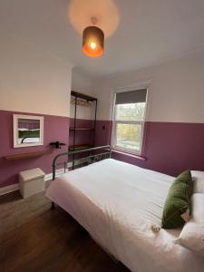 1 dormitorio con cama blanca y pared morada en The Little Place By The Sea, en Kent