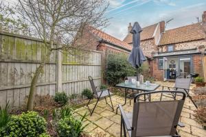 um pátio com uma mesa, cadeiras e um guarda-sol em Bracken Cottage em Brancaster