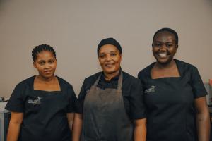 Tres mujeres juntas en una cocina. en Africa Awaits Lodge & Safaris, en Gobabis
