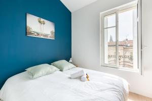 1 cama blanca con pared azul y ventana en Magnifiques Appartements Climatises En Plein Coeur Des Chartrons, en Burdeos