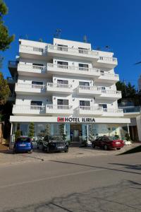 un gran edificio blanco con coches estacionados frente a él en Hotel Iliria en Sarandë
