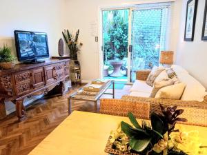 a living room with a couch and a tv at Palm Garden Villa-Apt - Tropical Oasis at Cronulla Beach in Cronulla