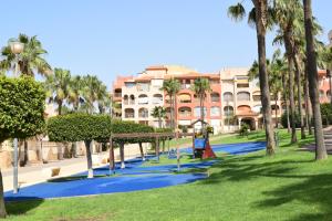 een speeltuin in een park met palmbomen en een gebouw bij Alta Entinas Almerimar .Modern apartment close to beach, beautiful pool. in El Ejido