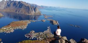 a woman sitting on the edge of a mountain overlooking a city at Lofoten - Koselig leilighet for 3 personer. in Sund +10 photos