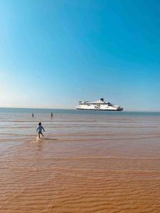 カレーにあるLa Félicita Calais Plageのクルーズ船を背景にビーチを歩く子供