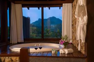 uma casa de banho com banheira e uma janela com copos de vinho em Maua Brasil Hotelaria em Visconde de Mauá