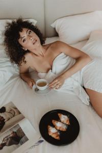 a woman laying in bed with a cup of coffee and food at Chanion One Suites by Good Life in Heraklio Town