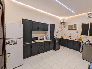 a kitchen with black cabinets and a white refrigerator at Madina Luxe Apartments - 7 minutes to Haram by Car - Mount Uhud Views - Free Parking - Kitchen in Al Madinah