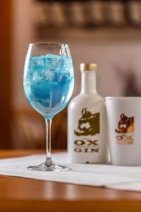 Hotel & Restaurant Zum Ochsen -Ox Distillery في هوسباخ: مشروب أزرق في كأس نبيذ بجوار زجاجة