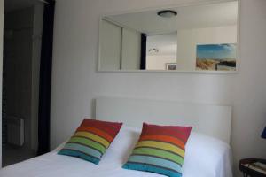 a white bed with two colorful pillows and a mirror at appartement cosy et nature au coeur du Bassin in Arès