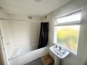 La salle de bains est pourvue d'un lavabo, d'une baignoire et d'une fenêtre. dans l'établissement Cosy two bedroom apartment,SE13, à Londres