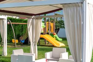 een speeltuin met een glijbaan en stoelen in het gras bij Domino Suite Hotel & Residence in Lido di Jesolo