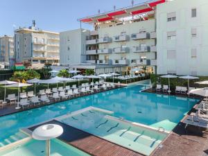 una piscina con sedie e ombrelloni accanto a un edificio di Domino Suite Hotel & Residence a Lido di Jesolo