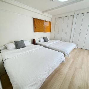 two beds in a room with white walls and wooden floors at Neighbor's Hotel 十日市 in Hiroshima