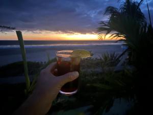 a hand holding a drink with a view of the beach at Stella Mar Oceanfront Hotel in Popoyo