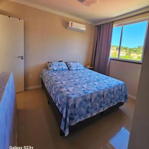 - une chambre avec un lit doté d'une couette bleue et d'une fenêtre dans l'établissement Cobertura em Bombinhas - Piscina - Luxo - Alto Padrão, à Bombinhas