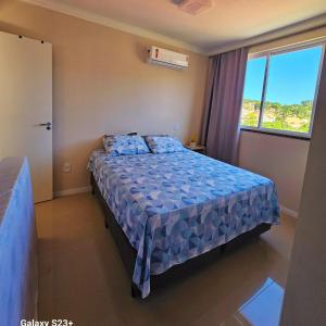 a bedroom with a bed with a blue comforter and a window at Cobertura em Bombinhas - Piscina - Luxo - Alto Padrão in Bombinhas +36 photos