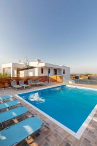 une piscine avec des chaises et une maison en arrière-plan dans l'établissement Villa Cleopatra Private Heated Pool, Tennis & Football, à Koskinou