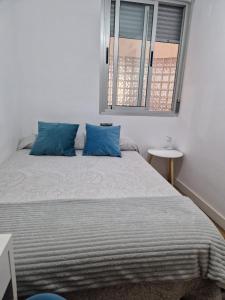 Un dormitorio con una cama con almohadas azules y una ventana en Quarto com banheiro privado em apartamento familiar, en Alicante