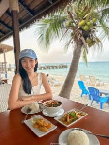 una mujer sentada en una mesa con comida en la playa en Samed Seaside Resort - เสม็ด ซีไซด์ รีสอร์ท, en Ko Samed