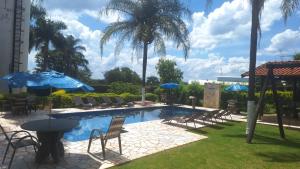 a swimming pool with chairs and a table and umbrellas at Hotel Green Village in Jardinópolis