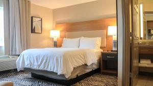 una camera d'albergo con letto con lenzuola e cuscini bianchi di Candlewood Suites - Peoria at Grand Prairie, an IHG Hotel a Peoria