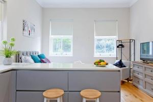una cocina blanca con fregadero y 2 taburetes en Bright and cheerful studio, en Londres