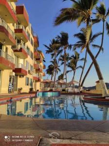 a swimming pool in front of a hotel with palm trees at Bonito y acogedor departamento Manzanillo in Manzanillo
