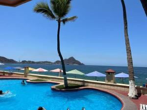 a swimming pool next to the ocean with palm trees at Bonito y acogedor departamento Manzanillo in Manzanillo
